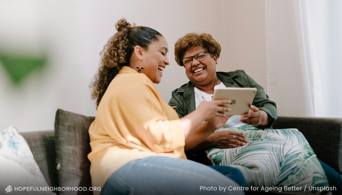 Two women sitting on a sofa, looking at something on a tablet.