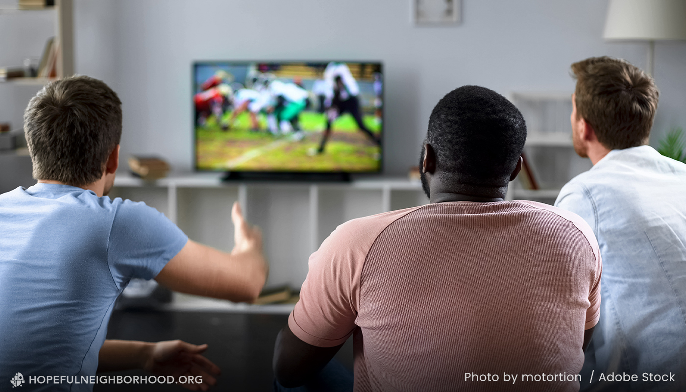 A group of 3 men sit in a living room watching sports on the tv.