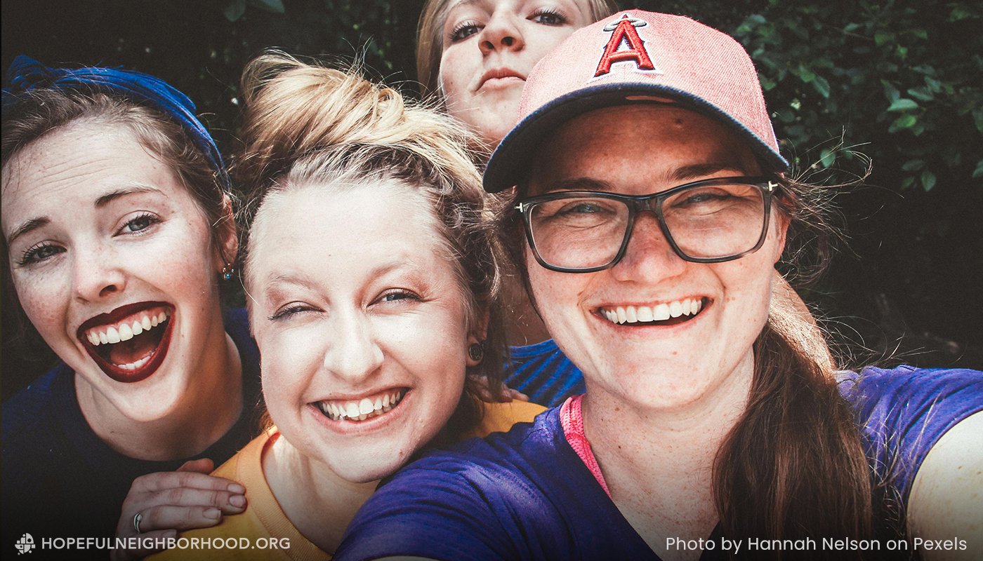 Three girls taking a selfie with a fourth girl trying to get in the picture from behind the girls.