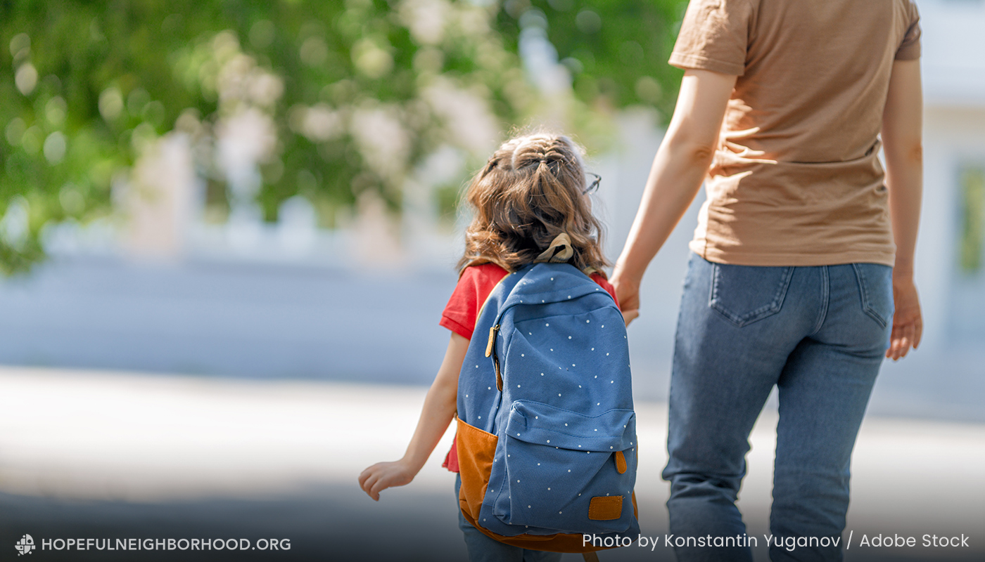 Photo of a mom holding her young daughter's hand on a walk to school.