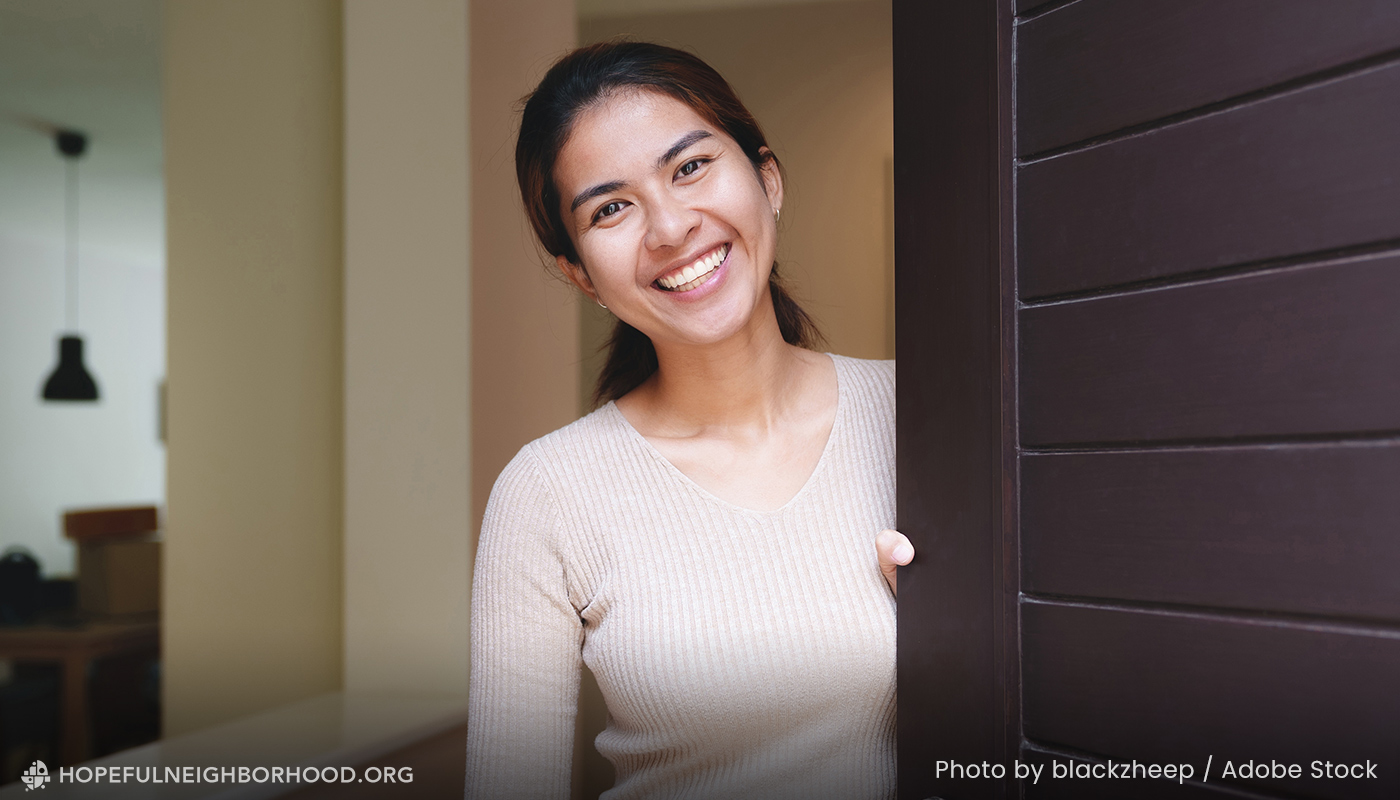 Photo of a friendly woman opening a front door to welcome someone in.