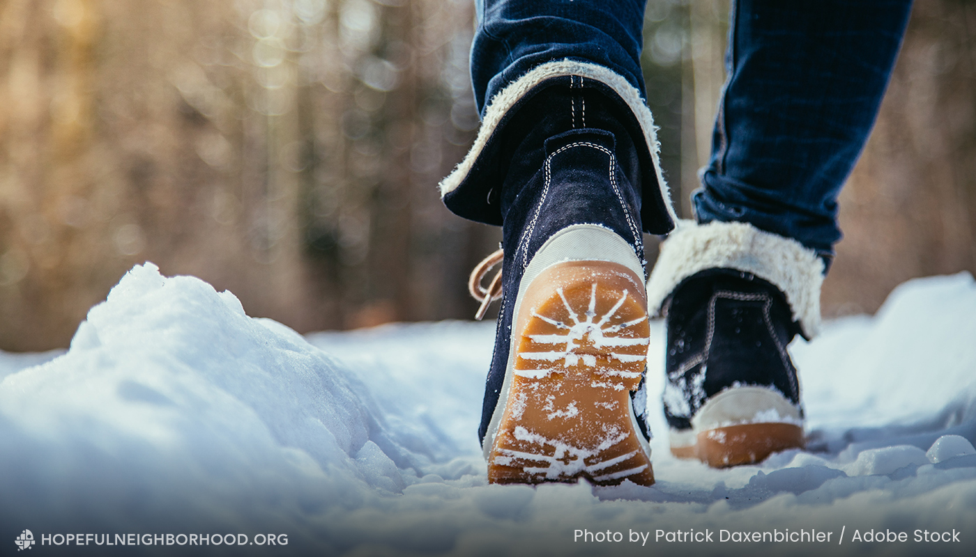 Photo of a person walking away from the camera in the snow. Photo only shows the back of the person, ankles and boots.